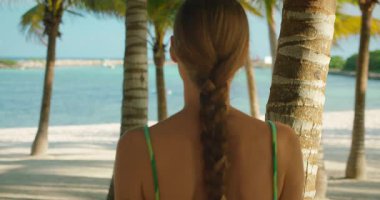 Meksika 'daki palmiye ağaçlarının arasından kumlu sahilde denize bakan örgülü bir kadın..