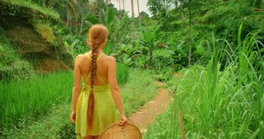 Yaz aylarında yemyeşil bitki örtüsüyle çevrili pirinç yolunda yürüyen bir kadın..