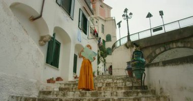 Atrani merdivenlerinde giyinmiş bir kadın haritaya bakıyor ve yaz sıcağında antik binalara bakıyor..