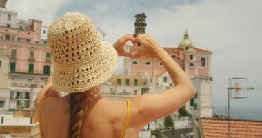 Kadın, Amalfi, Atrani, Amalfi sahillerindeki manzaralı bir sahil kasabasının önünde elleri ile bir kalp şekli oluşturur..