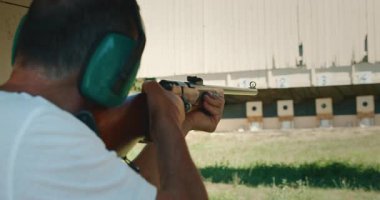 Kulaklık takan bir adam antrenman sırasında uzaktaki atış poligonuna nişan alıp ateş ediyor..