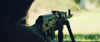 Atıcının elinde dürbünlü tüfek var. Gün ışığında dışarıdaki hedefe nişan alıyor..