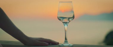 Terasta şarap kadehi, yaz günbatımının arka planda deniz üzerinde yansıması gibi..