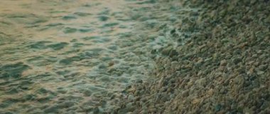 Hırvatistan 'da yazın alacakaranlıkta çakıllı plaj ve yumuşak deniz dalgalarının yakın görüntüsü.