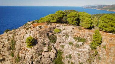 Kefalonya adasındaki bir tepeden İyon Denizi manzaralı kayalık sahil yolunda yürüyen kadın..
