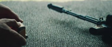 Adam, dışarıdaki ateşli silahların yanında, halı döşenmiş yerde tüfek mühimmatı organize ediyor..