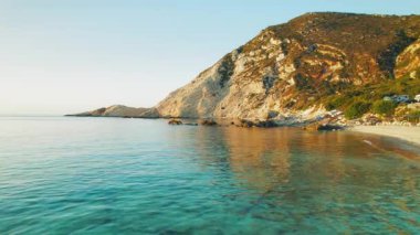 Akşam güneşi, kayalık kıyıları olan Yunanistan 'ın Kefalonia adasındaki Petani Sahili' ndeki sakin denizi yansıtıyor.