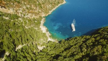 Yeşil kayalıklarla çevrili tenha bir turkuaz deniz koyuna demir atmış yelkenli..