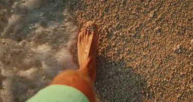 Makarska Hırvatistan 'da gün batımında çakıl taşı sahil şeridinde çıplak ayakla yürüyen adam.