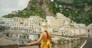 Bir kadın yaz günü pastel evlerle Atrani şehrinin yamaçtan manzarasını seyrediyor..