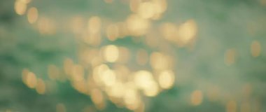 Deniz kenarında gün batımında su yüzeyine yansıyan altın bokeh ışıkları.