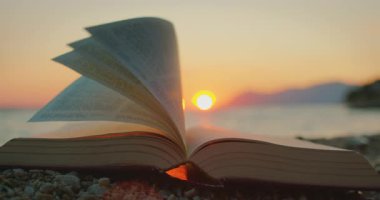 Yazın renkli günbatımında deniz esintisinde dönen açık kitapların sayfaları.