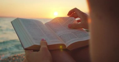 Günbatımında kutsal kitap okuyan kadın. Sayfalar dönüyor ve okyanus manzaralı..