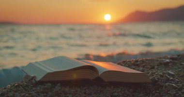 Açık kitap, Hırvatistan 'ın sakin manzarasında güneş okyanusun üzerinde batarken çakıl taşlarına dayanıyor.