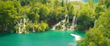 Turkuaz su yazın Plitvice Gölleri 'ndeki yemyeşil şelalelerin altından akar..