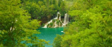 Geniş şelale ve mavi göl yaz ormanlarında yemyeşil yapraklarla çevrili..