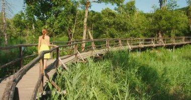Güneşli bir yaz gününde, bereketli Plitvice ormanında, tahta kaldırımda tek başına yürüyen bir kadın..