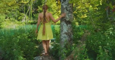 Çıplak ayaklı kadın, bereketli göl kenarındaki ağaç gövdesine dokunuyor Plitvice Park Hırvatistan 'daki turkuaz suyun yakınındaki ormanda yürüyor.