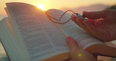 Gün batımında kumsalda elleri açık İncil kitabı ve ahşap haç tutuyor..