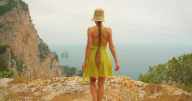 Yazın Capri 'de Faraglioni kayalıklarına ve denizlerine bakan uçurumun kenarında yürüyüş yapan bir kadın..