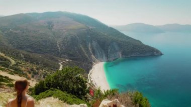 Kefalonya 'daki Myrtos Sahili' nde turkuaz deniz sularına bakan bir kadın gezgin görülüyor..