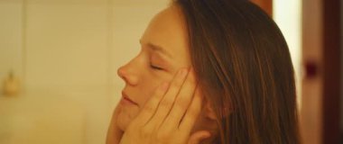 Kadın yüzüne nazikçe dokunuyor sıcak ışıkta gözleri kapalı..