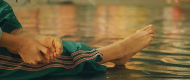 Sıcak bir ışıkta, yansıtıcı bir zeminde yalınayak uzanan bir insanın yakın çekimi..