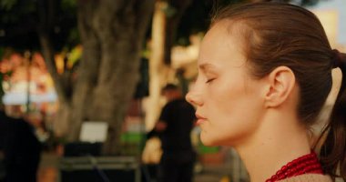 Sakin sakin nefes alan bir kadın, sakin şehir ortamında gözleri kapalı..