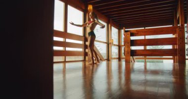 Dansçı, ahşap bir stüdyoda doğal ışık altında zarif bir duruş sergiliyor..