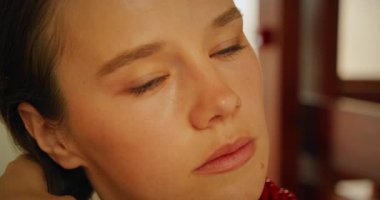 Banyoda saçlarını tarayan bir kadın kapalı alanda odaklanmış bir ifadeyle aynaya bakıyor..