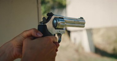 Atış menziline gümüş bir tabanca doğrultup ateş eden birinin yakın çekim görüntüsü..