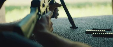 Tetikçi, açık hava menzilinde bipod destekli tüfekle hasırda yatıyor..