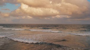 Okyanus dalgaları, Meksika 'daki dramatik bulutların altında gün batımını yansıtıyor..
