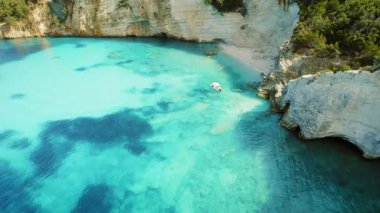 Yunanistan 'da yaz mevsiminde kayalık kıyıları yakınlarındaki parlak turkuaz suyun üzerinde yüzen tekne.