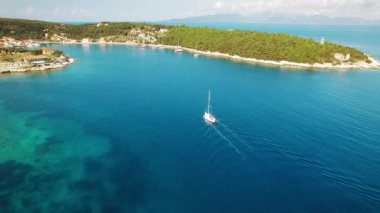 Yelkenli, yazın Kefalonia 'da Fiskardo ormanlarının kıyısında mavi körfezde geziyor..