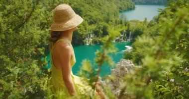 Yaz şapkalı kadın Plitvice Hırvatistan 'daki turkuaz göllere ve şelalelere hayran..