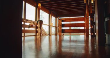 Kadın, üst kattaki ahşap dans stüdyosunun içinde korkuluk tutarak esniyor..