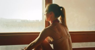 Güneş ışığında evde yoga yapan bir kadın, uzatılmış bacağını eliyle tutuyor..