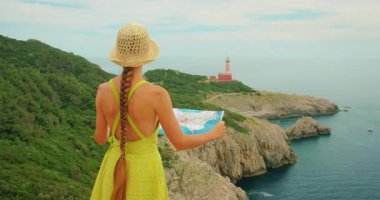 Elinde harita tutan kadın, Capri 'deki uçurumun kenarındaki deniz feneriyle manzarayı inceliyor..