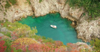 Capri 'nin kayalık kıyı bölgesinde yeşil koyda yüzen teknenin yüksek açılı görüntüsü.
