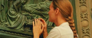 İtalya 'daki Duomo Milan Katedrali' nin bronz kapısında İsa ve Meryem 'in bronz bronz rengine dokunan kadın,.