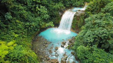 Şelale, Kosta Rika ormanlarında yürüyen bir kadınla turkuaz bir havuza akıyor..