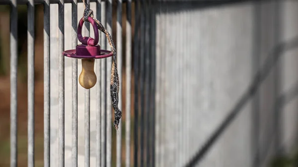 close up of a lost pacifier hanging on a metal fence as baby, child, security, protection, parenting, calmness concept with copy space and selective focus.