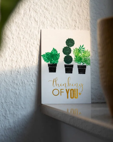 thinking of you card with illustrated plants on a windowsill illuminated by the sunlight at golden hour