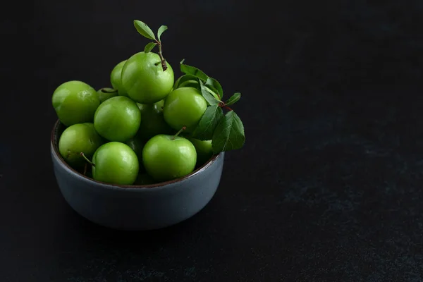 Green plum fruit in ceramic bowl on dark background, fruit that pregnant women love