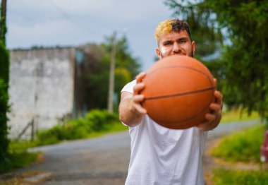 Basketbolcu basketbol topuyla poz veriyor iki eliyle tutuyor ve yüzüyle gözünü korkutmaya çalışıyor.