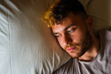 Genç adam pencereden dışarı bakarken yatakta dinleniyor.