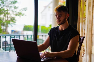 Pencereye yakın laptopla çalışan bir adam.