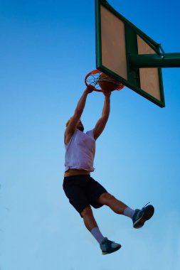 Basketbol oynayan ve mavi gökyüzünde smaç basan adam.