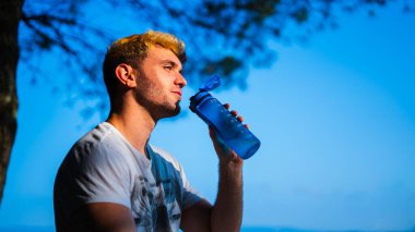 Genç adam açık havada mavi gökyüzü ile idmandan sonra susuz kalıyor.